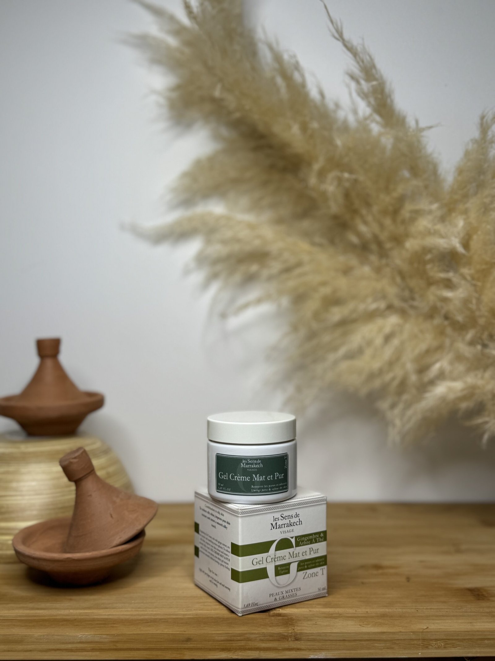 Pot et boîte du Gel Crème Mat et Pur Les Sens de Marrakech à l'étiquette verte, posés sur une surface en bois avec tajines en terre cuite et herbes de pampa en arrière-plan