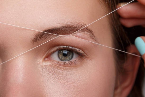 Épilation des sourcils au fil par une esthéticienne professionnelle