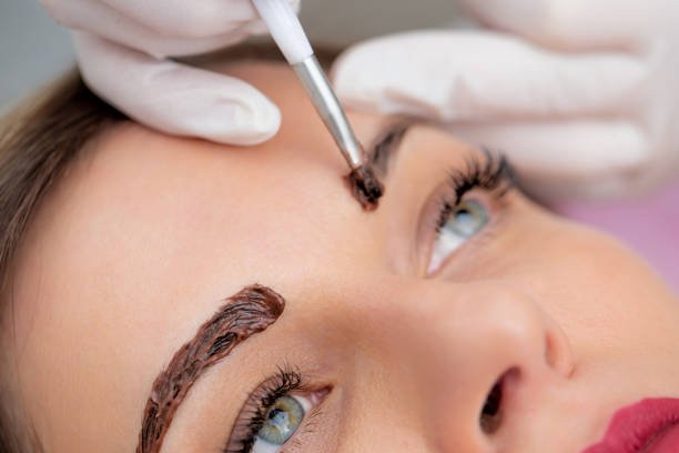 close up photo of beautician applying dye on woman's eyebrows