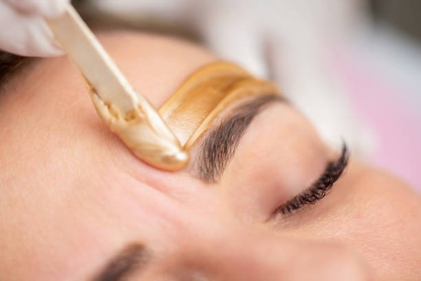 Épilation des sourcils à la cire dorée par une esthéticienne professionnelle